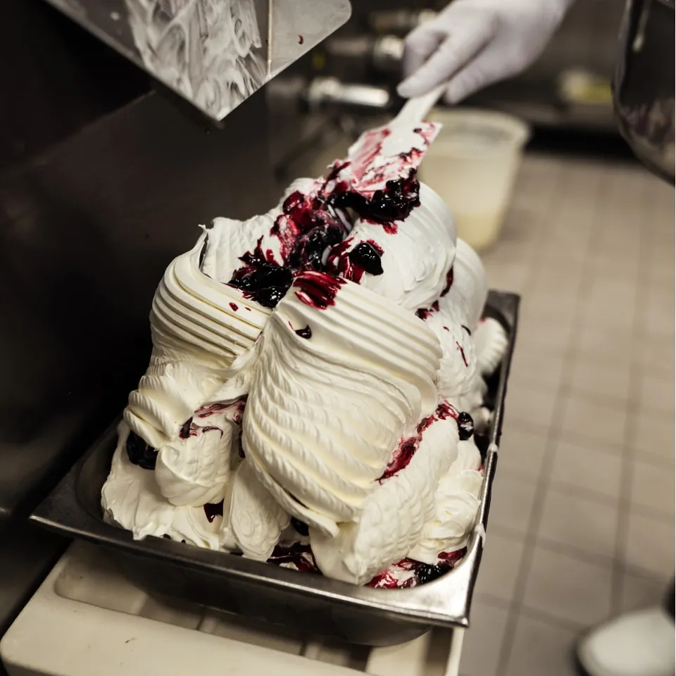 A gelatiere shaping fresh ice cream with berry sauce